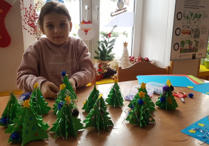 Dziewczynka pozuje z choinkami wykonanymi przez dzieci