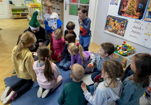 Studentka AWF siedzi z dziećmi na macie w sali i rozdaje im prezenty